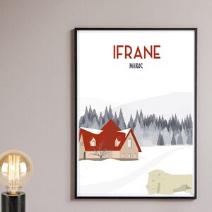 Könnte beinhalten: Ein Poster mit schwarzem Rahmen und weißem Hintergrund. Das Poster zeigt ein rotdachiges Haus in einem schneebedeckten Wald mit dem Text "IFRANE MAROC" oben. Im Vordergrund befindet sich eine weiße Löwenstatue.