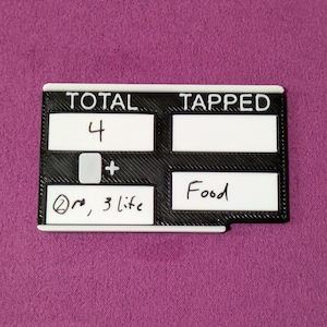 May include: A black and white game counter with the words "TOTAL" and "TAPPED" at the top. The counter has the number "4" written in the top left box, and the word "Food" in the bottom right box. The text "@re, 3 life" is written in the bottom left box.