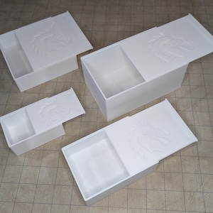 Puede incluir: Tres cajas blancas con diseños de dragones en las tapas. Las cajas son de diferentes tamaños y tienen una tapa deslizante.