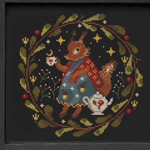 May include: Cross stitch pattern featuring a squirrel wearing a red and blue dress, holding a cup of tea, surrounded by a wreath of leaves and berries. The pattern is titled "Mama Witch Xstitch" and includes the text "Cross Stitch Patterns".