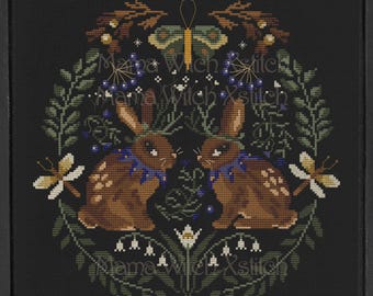 May include: Cross stitch pattern featuring two brown rabbits with blue floral collars, a butterfly, and a floral wreath on a black background. The pattern is titled "Mama Witch Xstitch".