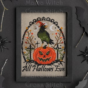 May include: A cross stitch pattern framed in black wood with a white background. The pattern depicts a black crow wearing a witch's hat perched on a jack-o-lantern with a spooky face. The text "All Hallows Eve" is stitched below the jack-o-lantern.