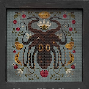 Puede incluir: Arte de punto de cruz que presenta un pulpo marrón con ojos grandes, rodeado de motivos florales y frutales en rojo, amarillo y blanco. La obra está enmarcada en un marco de madera negro, sobre un fondo azul apagado.