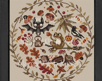 Op de afbeelding: Borduurpatroon met een fantasierijk boslandschap met een vleermuis, een kikker, een vogel en paddenstoelen. Het patroon is omgeven door een krans van bladeren en bessen. De tekst "Mama Witch Xstitch" staat bovenaan het patroon.