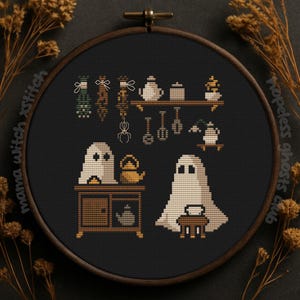 May include: Cross-stitch embroidery in a wooden hoop depicting a spooky kitchen scene. The design includes two ghosts, a cabinet, a shelf with teapots, and hanging decorations. The colour palette is primarily black, brown, and cream.