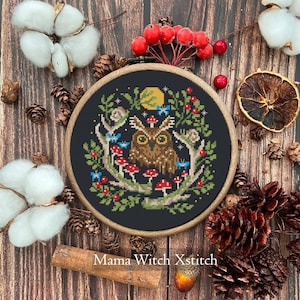 May include: A cross-stitch embroidery featuring a brown owl with yellow eyes, surrounded by red mushrooms, blue butterflies, and green foliage, set against a black background. The design is framed in a wooden hoop, with the text "Mama Witch Xstitch".