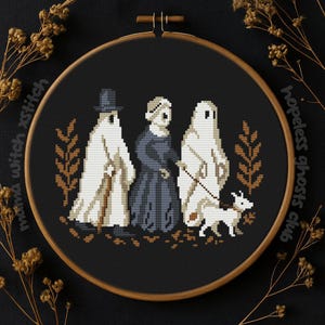 以下が含まれることがあります： 木製のフレームに入ったクロスステッチ刺繍。黒い背景に3体の幽霊のような人物と犬が描かれています。人物は白とグレーで、一人は帽子をかぶり、もう一人はドレスを着ています。「hopeless ghosts club」の文字が見えます。