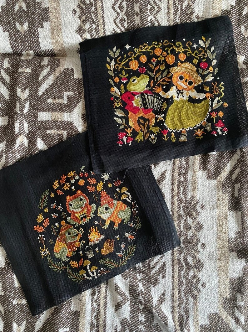 May include: Two black fabric panels with embroidered images. The top panel features a frog playing an accordion and a girl in a green dress. The bottom panel features three frogs around a campfire.