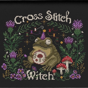 May include: Cross Stitch Witch pattern featuring a green frog wearing a party hat and holding a mushroom. The frog is surrounded by green foliage, purple flowers, and the text "Cross Stitch Witch".