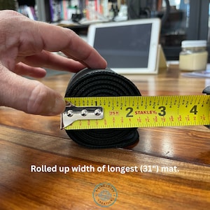 May include: A black yoga mat rolled up and measured with a yellow tape measure. The tape measure reads 31 inches. The text "Rolled up width of longest (31") mat." is below the image.