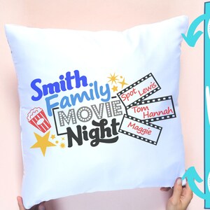 Puede incluir: Una almohada blanca con un dise&ntilde;o azul, rojo y amarillo que dice "Smith Family Movie Night". Tambi&eacute;n hay cuatro tiras de pel&iacute;cula con nombres en ellas: Spot Lewis, Tom, Hannah y Maggie.