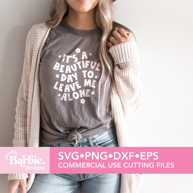 May include: A gray t-shirt with a pink graphic that says "It's a beautiful day to leave me alone." The graphic is surrounded by small pink flowers. The shirt is being worn by a person with a white cardigan and blue jeans.