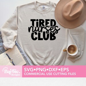 Może przedstawiać: Biała bluza z nadrukiem "TIRED NURSES CLUB" czarnymi literami. Bluza leży płasko na powierzchni z brązowym kapeluszem i kubkiem do kawy.
