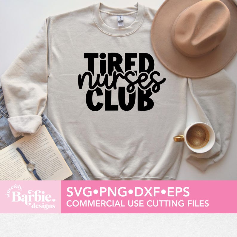 Może przedstawiać: Biała bluza z nadrukiem "TIRED NURSES CLUB" czarnymi literami. Bluza leży płasko na powierzchni z brązowym kapeluszem i kubkiem do kawy.