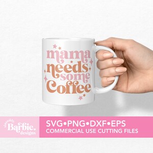 Op de afbeelding: Een witte keramische mok met de tekst "mama needs some coffee" in roze en bruine letters met sterren.