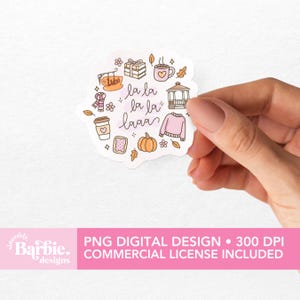 May include: A die-cut sticker with a whimsical design featuring autumn-themed illustrations. The sticker includes a pumpkin, sweater, coffee cup, and the text "la la laaa". The sticker is held by a hand.