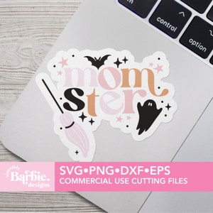 以下が含まれることがあります： ピンクとオレンジの文字で「momster」と書かれた白いステッカー。ステッカーには、黒いコウモリ、幽霊、ピンクのほうきも描かれています。