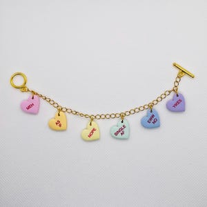 May include: A gold chain bracelet with colorful heart charms. Each charm has a different message, including "Meh", "As If", "Nope", "Single AF", "Eww No", and "Yikes".