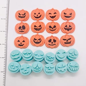 May include: Orange and black Halloween-themed decorations. The image features several orange pumpkin-shaped decorations with carved faces, and blue circular decorations with various spooky faces. These are likely for crafting or decorating.
