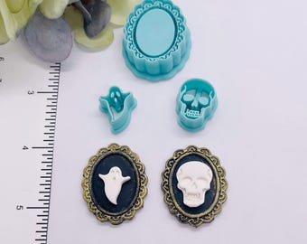 Può includere: Una collezione di materiali per il fai-da-te a tema Halloween. Include uno stampo ovale turchese, formine per biscotti a forma di fantasma e teschio e due spille ovali con disegni di fantasmi e teschi. Le spille hanno uno sfondo nero e cornici dorate.