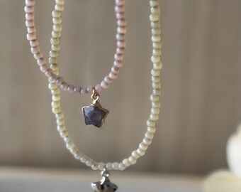Peut inclure: Deux colliers superposés avec des breloques en forme d'étoile. Le collier du haut est composé de perles de couleur lilas clair et le collier du bas est composé de perles de couleur vert clair. Les deux colliers ont un pendentif en forme d'étoile avec une pierre violette.