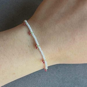 May include: A white beaded bracelet with red and green beads. The bracelet is on a person's wrist.