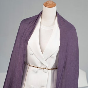 May include: A white blazer with a double breasted closure and a gold chain belt. A purple scarf is draped over the blazer.