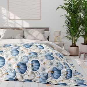May include: A bedspread featuring a repeating pattern of blue and white pumpkins with gold stems and floral accents on a white background. The bedding is draped over a bed with gray pillows and a wooden headboard. The room is decorated with plants.