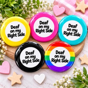 May include: Five circular pin-back buttons featuring a white center with the black text 'Deaf on my Right Side'. The buttons have yellow, pink, teal, black, and rainbow-striped borders, each displaying the same text clearly in a bold font.