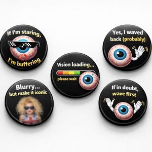 Peut inclure: Ensemble de cinq boutons ronds noirs avec des motifs humoristiques sur le thème des yeux. Un bouton présente un œil avec des lunettes de soleil et le texte "If I'm staring, I'm buffering." D'autres boutons affichent des phrases comme "Vision loading..."