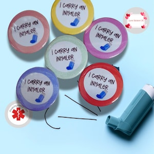 May include: Five colourful round buttons with the text "I carry an inhaler" and a cartoon image of an inhaler. The buttons are arranged in a circle around a blue inhaler.