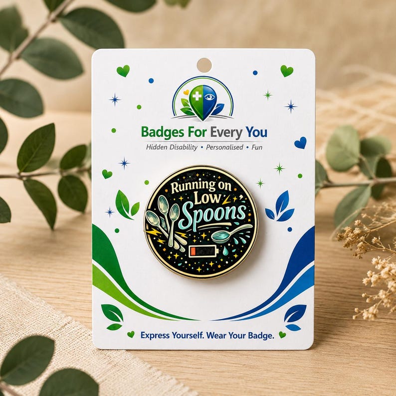 Puede incluir: Un pin redondo de esmalte sobre una tarjeta blanca con el texto Running on Low Spoons, ilustraciones de tres cucharas y un icono de bater&iacute;a baja. El pin tiene un fondo negro con estrellas doradas. La tarjeta incluye el texto Badges For Every You.