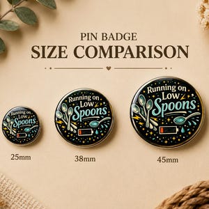 Puede incluir: Tres chapas circulares de 25mm, 38mm y 45mm. Cada chapa negra presenta el texto "Running on Low Spoons" en azul claro y blanco, con ilustraciones de cucharas plateadas, un icono de bater&iacute;a baja y peque&ntilde;as estrellas amarillas.