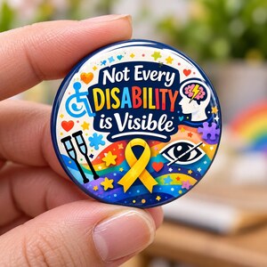 Puede incluir: Un botón redondo con el texto Not Every DISABILITY is Visible en letras azul oscuro y multicolores. El diseño incluye un icono de silla de ruedas azul, un lazo de concienciación amarillo, muletas, un cerebro, un ojo y estrellas.