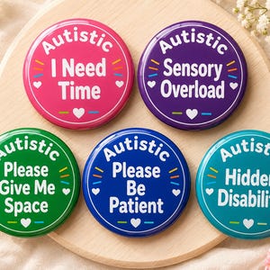 May include: Five circular pin-back badges in pink, purple, green, blue, and teal. Each badge features the word Autistic at the top, followed by phrases: I Need Time, Sensory Overload, Please Give Me Space, Please Be Patient, and Hidden Disability.