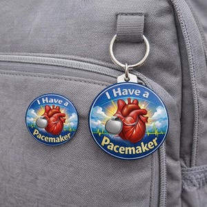 Puede incluir: Un botón y un llavero azules con el texto "I Have a Pacemaker". El botón y el llavero presentan un corazón rojo con un marcapasos, sobre un fondo de cielo con una línea de latidos.