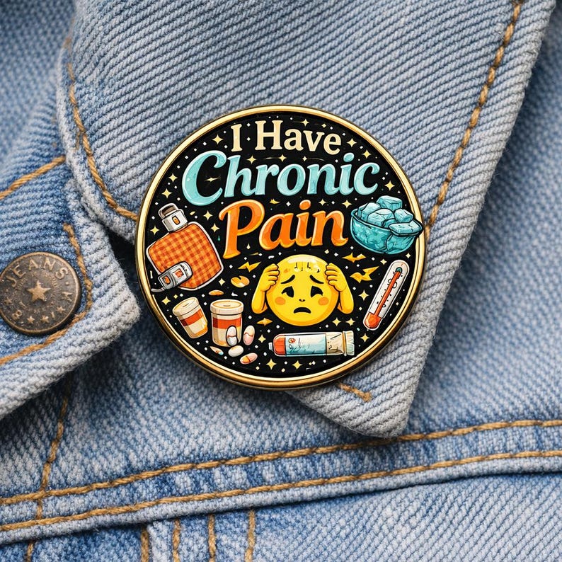 Puede incluir: Un pin redondo de esmalte con fondo negro que presenta el texto I Have Chronic Pain en azul claro y naranja. El dise&ntilde;o incluye un emoji amarillo triste, una bolsa de agua caliente a cuadros naranja, un cuenco azul con hielo, un term&oacute;metro y frascos.