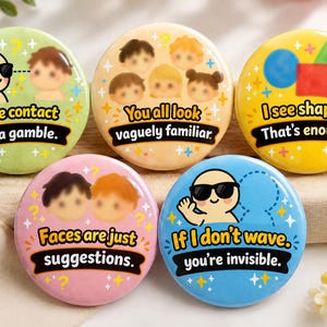 May include: Five round pinback buttons with colourful backgrounds and cartoon illustrations. Text includes: Eye contact is a gamble, You all look vaguely familiar, I see shapes. That's enough, Faces are just suggestions, and If I don't wave, you're invisible.