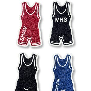 May include: Four glittery wrestling singlets with white trim, arranged in a grid. The red singlet features the name SHAW, the black singlet features MHS, and the blue singlet features CONNOR. The top center includes the text KOZEN MUM DESIGNS.