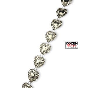 May include: A vertical trim strip featuring a series of silver-toned heart-shaped embellishments, each bordered by small reflective studs. The design includes a logo with the text KOZEN Mum DESIGNS. The hearts are connected by thin silver wire.