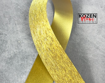 May include: A gold ribbon with a textured surface is looped against a gray background. The ribbon has a metallic sheen and is labeled with the text "KOZEN Mum DESIGNS" in a black and red font.