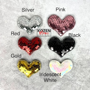 May include: A collection of heart-shaped sequin patches in silver, pink, red, black, gold, and iridescent white. Each heart is outlined with a matching border. The text "Silver", "Pink", "Red", "Black", "Gold", and "Iridescent White" is displayed above each heart.
