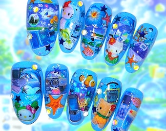 May include: A set of ten blue press-on nails featuring various designs including Hello Kitty characters, tropical fish, starfish, flowers, retro mobile phones, and computer icons, accented with small star-shaped sequins and clear rhinestones.