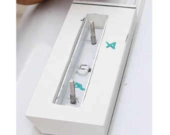 May include: White rectangular block with two silver screws protruding from the top. The block has a rectangular opening with a silver metal piece inside. The block has a green "X" written on it.
