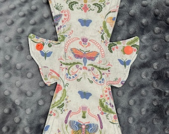 May include: A reusable cloth menstrual pad with a cream-colored background. The pad features a colorful butterfly and floral pattern in shades of blue, pink, green, and purple. Two orange snaps secure the wings of the pad.