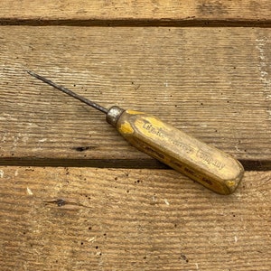 May include: A vintage wood handled awl with a metal point. The handle is labeled "The Utica Heater Company" and "FORGED  MADE IN USA 6405".
