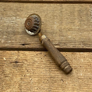 May include: A vintage wooden-handled metal cookie press with a fluted design. The press is rusty and has a worn wooden handle.