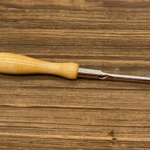 May include: A wooden handled crochet hook with a metal needle and a small loop at the end.