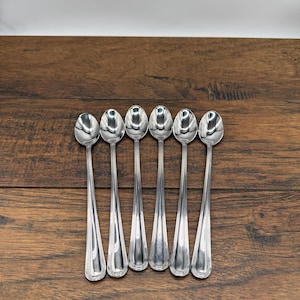 May include: Set of six silver spoons with rounded ends. The spoons are arranged in a row on a wooden surface.