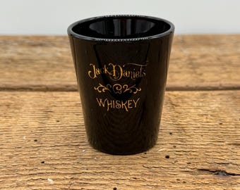 May include: Black shot glass with gold lettering that reads "Jack Daniel's Whiskey".